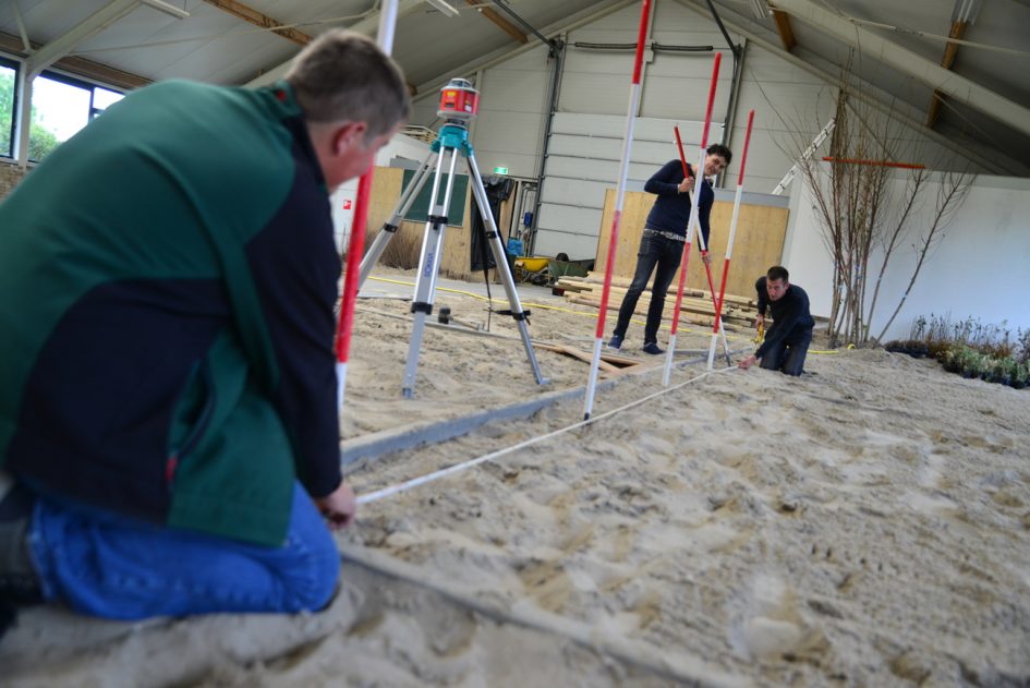 Drie mannen zijn aan het landmeten in een praktijkhal