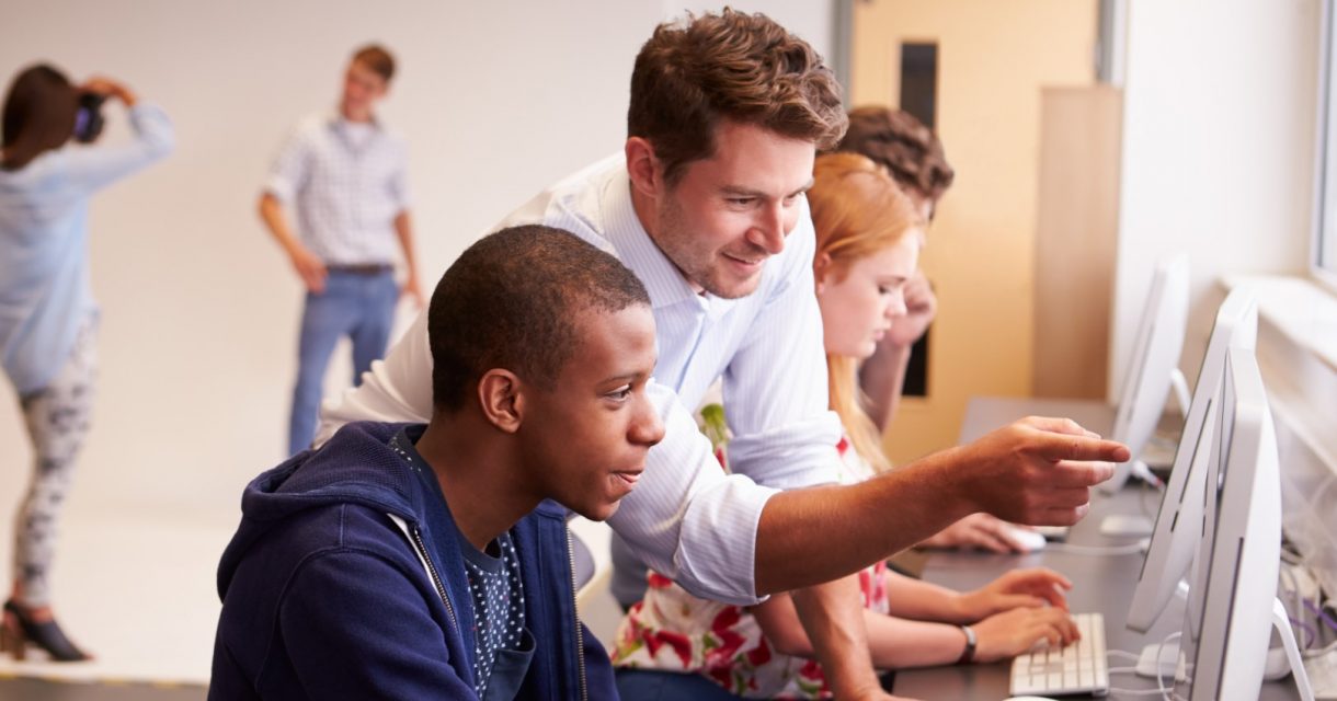 Man wijst iets aan op computerscherm voor student