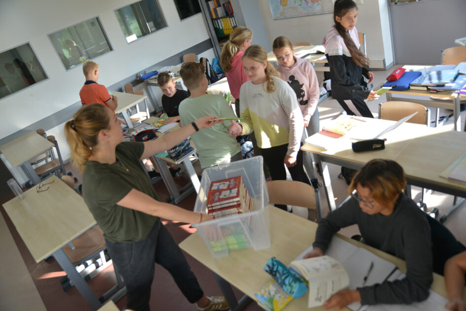 Foto docent deelt boeken uit aan leerlingen op pagina Ouderklankbordgroep